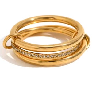 Peut inclure: Une bague dorée avec un design superposé. La bague comporte trois anneaux, dont un orné de petits pierres précieuses transparentes. La bague a une finition lisse et polie et une esthétique moderne.