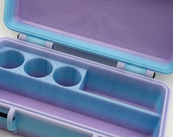 May include: Open, two-tone blue and purple storage box. The box has a rectangular shape with rounded corners and a hinged lid. Inside, there are compartments and circular holders. The interior is a lighter shade of purple, while the exterior is a gradient of blue and purple.