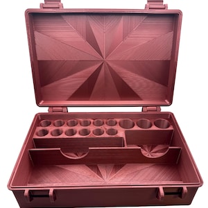 May include: Open, red-brown toolbox with an organized interior. The case is rectangular with a hinged lid and a latch closure. Inside, there are various compartments and cylindrical holders for tools or small items. The interior features a geometric starburst design.