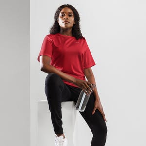 May include: A bright red short-sleeved t-shirt with a small white logo on the chest, paired with solid black athletic pants and a clear plastic water bottle with a dark grey lid, featuring a smooth texture and a standard crew neckline design.