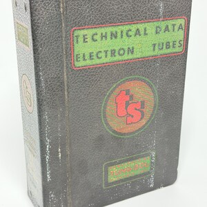 May include: A vintage black binder with the text "TECHNICAL DATA ELECTRON TUBES" in green and red. The binder has a textured surface and a circular logo with the letters "ts". The binder is slightly worn.