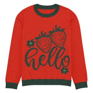 May include: Red long-sleeved sweater with a green collar and cuffs. The front features two strawberries and the word "hello" in green script, along with two green flower accents. A casual, comfortable top.
