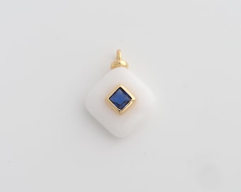 May include: A white, square pendant with a gold-coloured bail. The pendant features a square, deep blue gemstone set in a gold-coloured bezel. The pendant is likely for a necklace or bracelet.