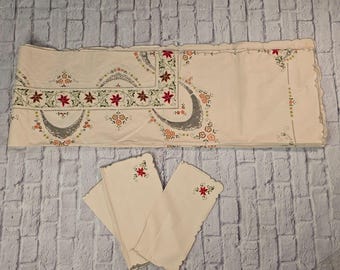 Può includere: Tovaglia color crema e tovaglioli abbinati con ricami floreali. La tovaglia ha un bordo smerlato e presenta fiori rossi, verdi e arancioni. I tovaglioli hanno un singolo fiore ricamato.