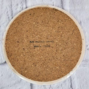 May include: Circular coaster with a cork base and a white ceramic edge. The cork surface has a textured appearance. The text "ALAN WALLWORK CERAMICS MADE IN ENGLAND" is printed on the cork surface.