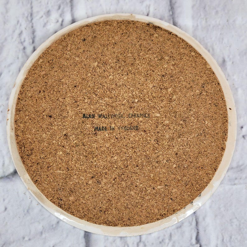 May include: Circular coaster with a cork base and a white ceramic edge. The cork surface has a textured appearance. The text "ALAN WALLWORK CERAMICS MADE IN ENGLAND" is printed on the cork surface.