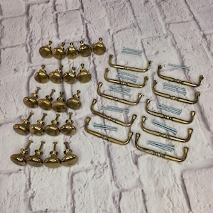 May include: A collection of brass-toned cabinet hardware including twenty round knobs and eight arched drawer pulls. Each piece is accompanied by matching silver-toned metal mounting screws. The hardware features a smooth, polished finish.