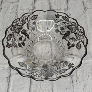 Könnte beinhalten: Eine klare Glasschüssel mit gewelltem Rand und silbernem Rand. Die Schüssel ist mit einem schwarzen Blumen- und Beerenmuster verziert. Die Schüssel ist rund und hat ein dekoratives Design.