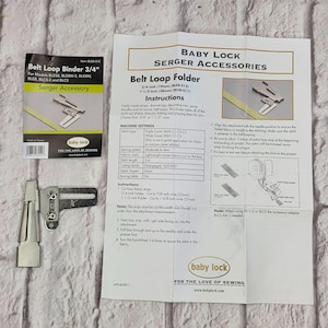 Peut inclure: Un guide-passepoil en métal argenté pour surjeteuse, accompagné de son emballage d'origine noir et jaune et d'une notice explicative blanche intitulée Baby Lock Serger Accessories Belt Loop Folder avec des schémas techniques.