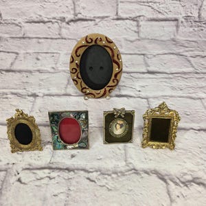 May include: Five ornate picture frames in various shapes and sizes. The frames are gold, bronze, and silver, with oval, square, and rectangular openings. Some frames have decorative embellishments, including rhinestones and mother-of-pearl.
