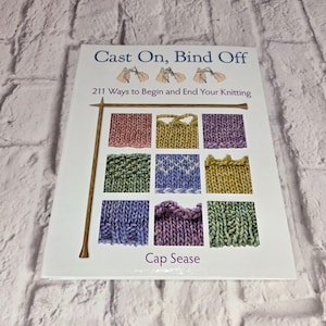 May include: A softcover book titled Cast On, Bind Off: 211 Ways to Begin and End Your Knitting by Cap Sease. The white cover features illustrations of knitting techniques and a grid of nine colourful knitted swatches with a wooden needle.