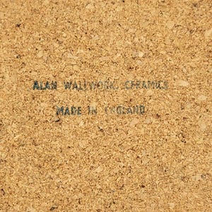 May include: A close-up of a cork coaster with the text "ALAN WALLWORK CERAMICS" and "MADE IN ENGLAND" printed in dark grey. The coaster has a textured, speckled surface.