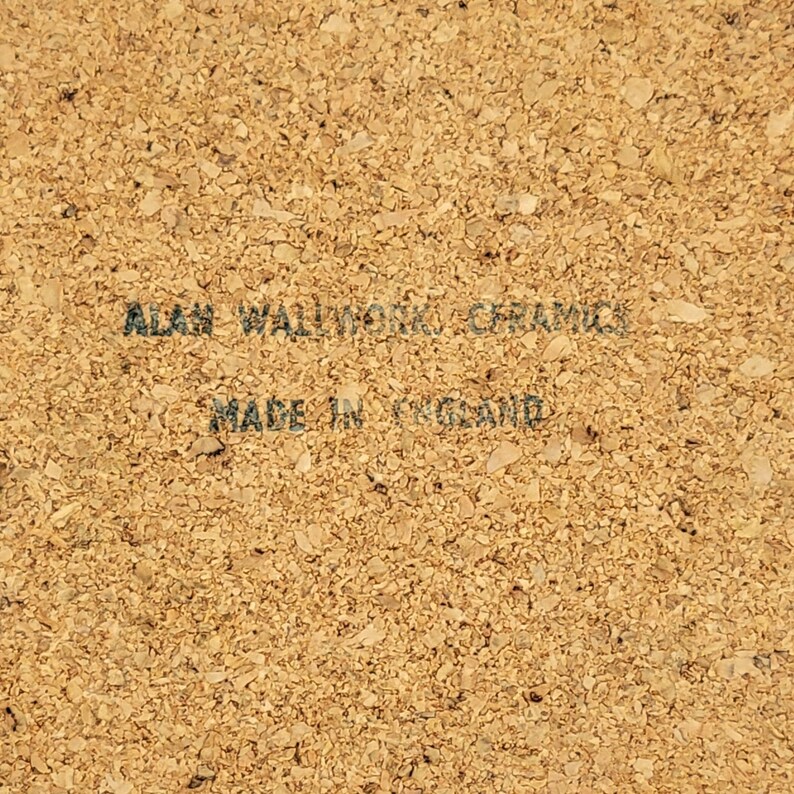 May include: A close-up of a cork coaster with the text "ALAN WALLWORK CERAMICS" and "MADE IN ENGLAND" printed in dark grey. The coaster has a textured, speckled surface.