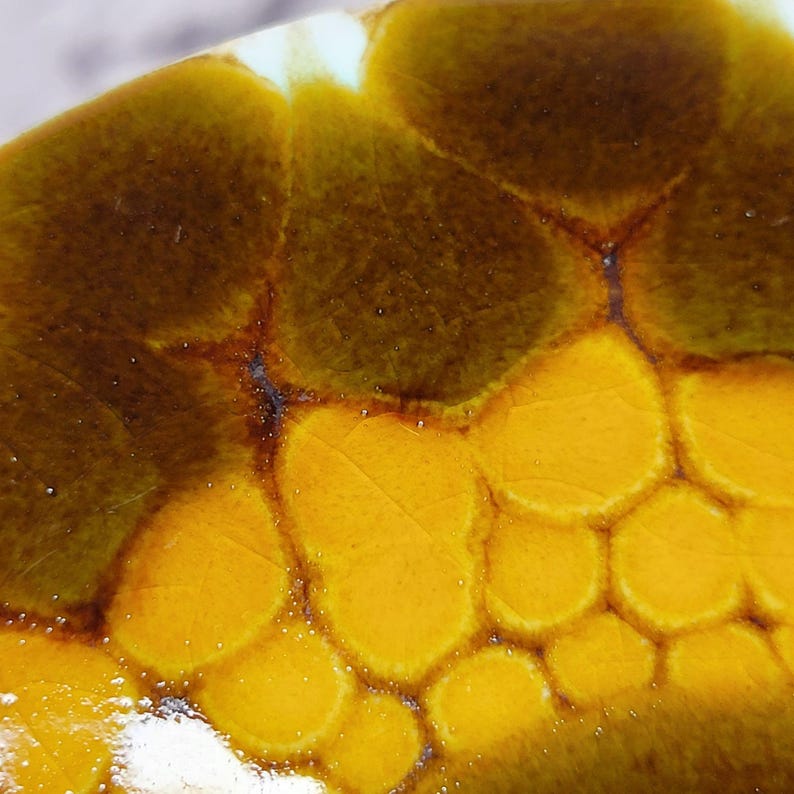 May include: Close-up of a ceramic surface with a distinctive pattern. The design showcases a blend of brown and yellow tones, producing a textured, organic look. The colours merge, forming a visually engaging abstract design.