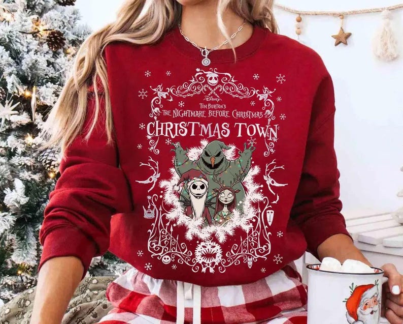 May include: A red sweatshirt featuring characters from "The Nightmare Before Christmas." The design includes Jack Skellington, Sally, and Oogie Boogie, with the words "Christmas Town" in a decorative frame. The sweatshirt has long sleeves.