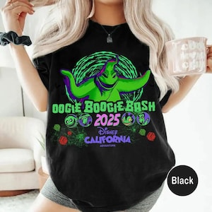 Op de afbeelding: Een zwart t-shirt met een felgroene afbeelding van Oogie Boogie uit The Nightmare Before Christmas. Het ontwerp bevat de tekst Oogie Boogie Bash 2025, Disney California Adventure en kleine illustraties van dobbelstenen, spinnenwebben en personages.