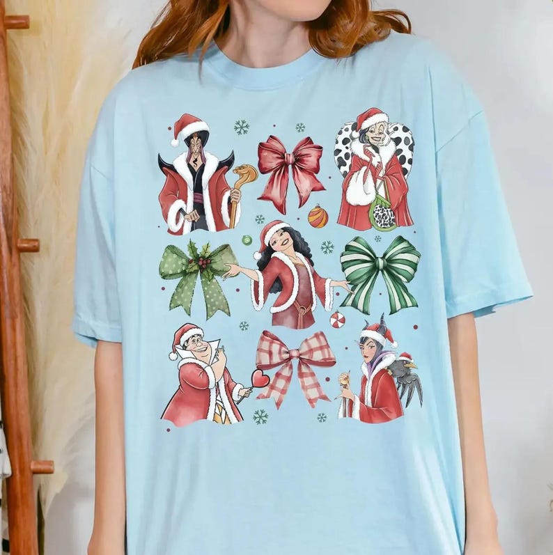 Op de afbeelding: Lichtblauw T-shirt met een feestelijk ontwerp. Het ontwerp toont cartoonfiguren in kerstmutsen en rode jassen, samen met strikken en sneeuwvlokken. Het shirt is gemaakt van een zacht materiaal.