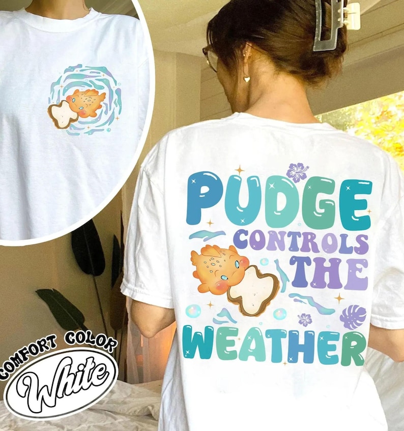 K&ouml;nnte beinhalten: Wei&szlig;es Comfort Color T-Shirt mit Grafik auf Vorder- und R&uuml;ckseite. Die Grafik auf der Vorderseite zeigt eine Cartoon-Kreatur in einem Wirbel. Die Grafik auf der R&uuml;ckseite zeigt "Pudge Controls The Weather" mit einer passenden Cartoon-Kreatur.