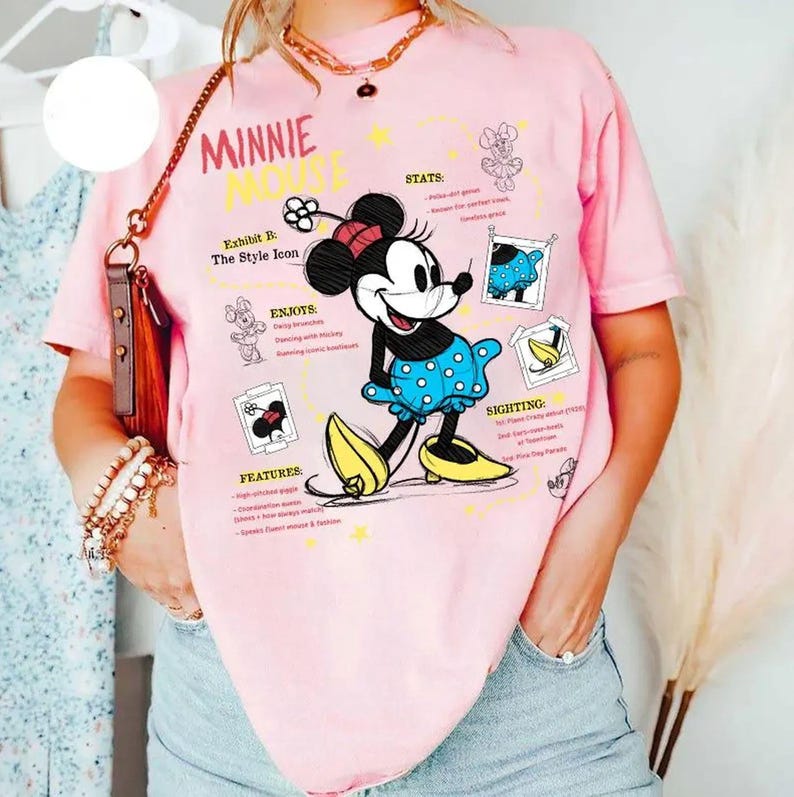 以下が含まれることがあります： 水玉模様の青いドレスと黄色の靴を履いたミニーマウスが描かれたピンクのTシャツ。「MINNIE MOUSE」の文字と「Exhibit B: The Style Icon」などのグラフィック要素が含まれています。
