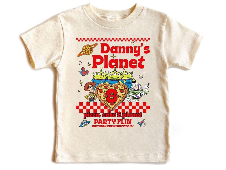 Pu&ograve; includere: T-shirt color crema con un design grafico colorato. Il design include il testo "Danny's Planet" in rosso, personaggi dei cartoni animati e un otto a forma di pizza. La maglietta ha anche il testo "Pizza, Cake & Planet PARTY FLIN BIRTHDAY CREW SINCE 2016!"
