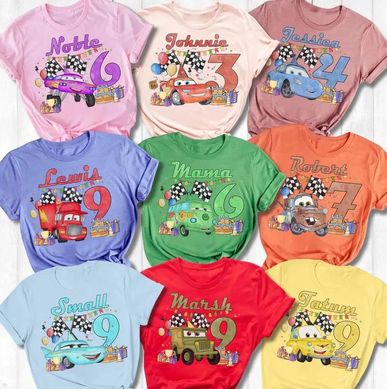 May include: A collection of colorful t-shirts featuring cartoon car graphics, names, and numbers. Each shirt has a different color and design, with names like "Noble", "Johnnie", and "Jessica". The shirts are likely for a birthday or special event.