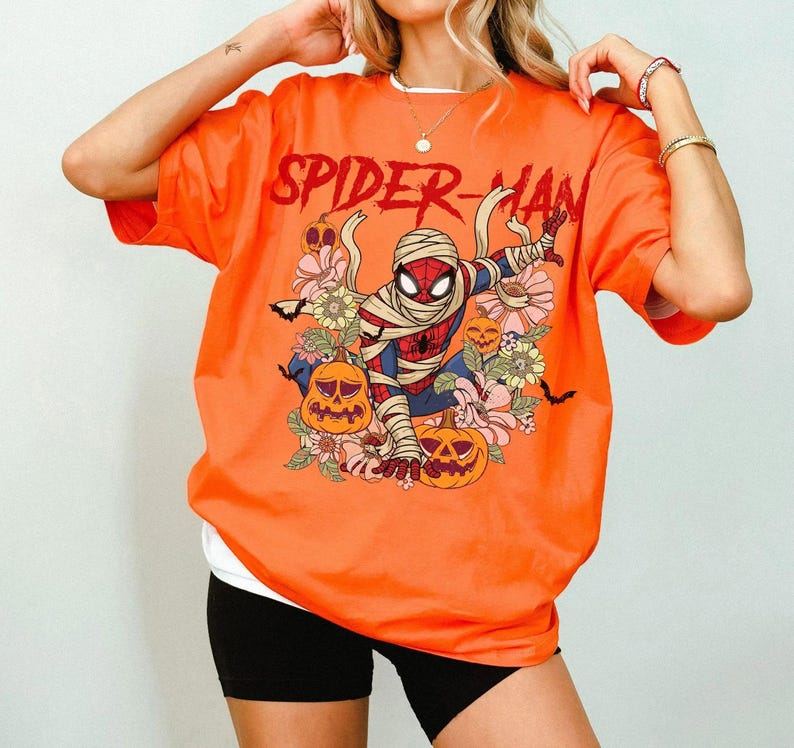 K&ouml;nnte beinhalten: Orangefarbenes T-Shirt mit dem roten Schriftzug "SPIDER-MAN". Die Grafik zeigt Spider-Man als Mumie, umgeben von K&uuml;rbissen und Blumen. Das Shirt hat ein wei&szlig;es Unterhemd und schwarze Shorts.