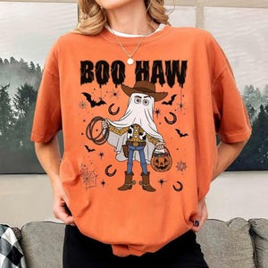 May include: A white ceramic mug with a black handle and the text "But First, Coffee" in a bold, black font. The mug is set against a blurred background, suggesting a cosy setting.