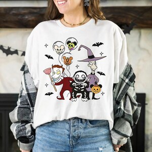 May include: White t-shirt with a colourful graphic of characters from The Nightmare Before Christmas. The design includes Jack Skellington, Sally, and other Halloween Town residents, along with bats and balloons. A fun, festive design for fans of the movie.