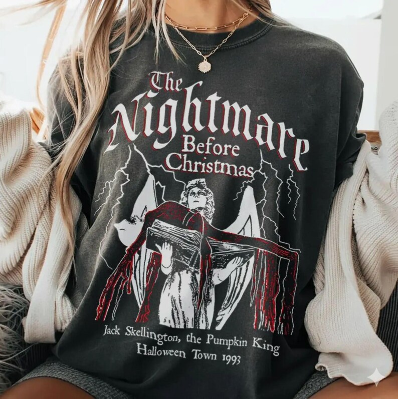 May include: Dark gray sweatshirt featuring the text "The Nightmare Before Christmas" in white and red, with an illustration of a character from the movie. The text "Jack Skellington, the Pumpkin King Halloween Town 1993" is also printed on the shirt.