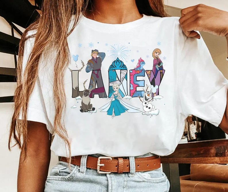 May include: White t-shirt with the word "LARKEY" in colourful, stylised letters. Each letter is decorated with characters from a popular animated film, including a reindeer, a snowman, and a princess.