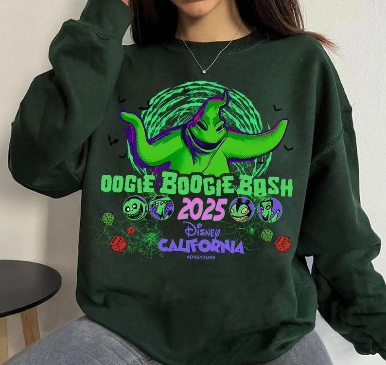 Op de afbeelding: Een donkergroen sweatshirt met lange mouwen en een afbeelding van het personage Oogie Boogie in felgroen. De tekst luidt Oogie Boogie Bash 2025 Disney California Adventure, vergezeld door kleine ronde karakterpictogrammen, dobbelstenen en spinnenwebben.