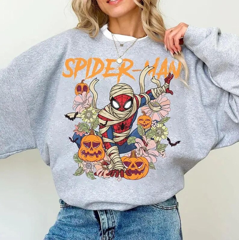 K&ouml;nnte beinhalten: Graues Sweatshirt mit einem Halloween-Thema Spider-Man-Design. Die Grafik zeigt Spider-Man in Bandagen, K&uuml;rbissen, Blumen und dem orangefarbenen Text "SPIDER-MAN".