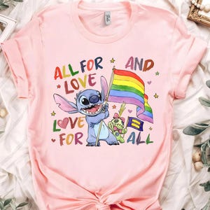 May include: Pink t-shirt featuring a cartoon character holding a rainbow flag. The shirt has the text "ALL FOR LOVE" and "LOVE FOR ALL" in a colorful design. The design includes stars and a second character.