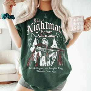 May include: Dark green t-shirt featuring the text "The Nightmare Before Christmas" in white, with an illustration of Jack Skellington. The graphic includes lightning bolts and the text "Jack Skellington, the Pumpkin King Halloween Town 1993".