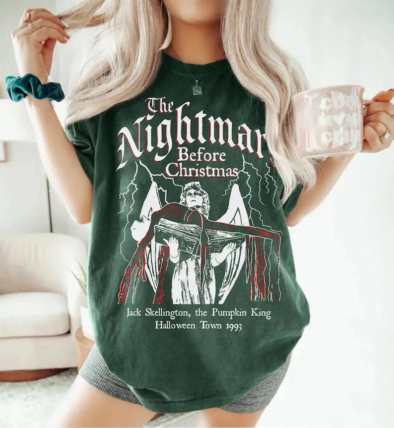 May include: Dark green t-shirt featuring the text "The Nightmare Before Christmas" in white, with an illustration of Jack Skellington. The graphic includes lightning bolts and the text "Jack Skellington, the Pumpkin King Halloween Town 1993".