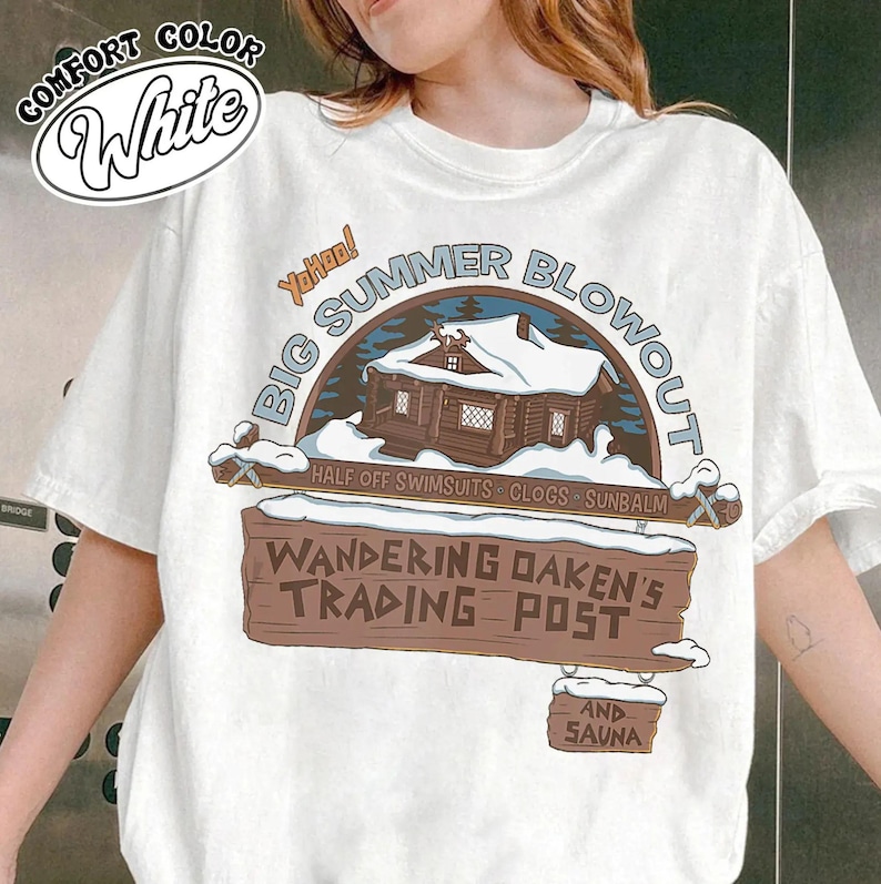 Op de afbeelding: Wit T-shirt met een afbeelding van een met sneeuw bedekte hut en de tekst "BIG SUMMER BLOWOUT". Daaronder staat op een houten bord "WANDERING OAKEN'S TRADING POST AND SAUNA". Het shirt heeft ook de tekst "HALF OFF SWIMSUITS - CLOGS - SUNBALM".