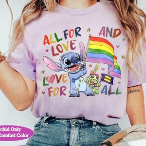 May include: A light purple t-shirt with the text "ALL FOR LOVE AND LOVE FOR ALL" and a cartoon character holding a rainbow flag. The shirt also features a smaller character and stars.