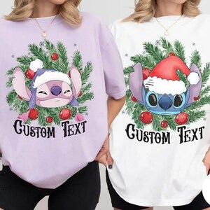 Puede incluir: Dos camisetas, una lavanda y otra blanca, con un personaje de dibujos animados que lleva un gorro de Pap&aacute; Noel y una corona navide&ntilde;a. El texto "CUSTOM TEXT" est&aacute; impreso debajo del personaje en una fuente estilizada.