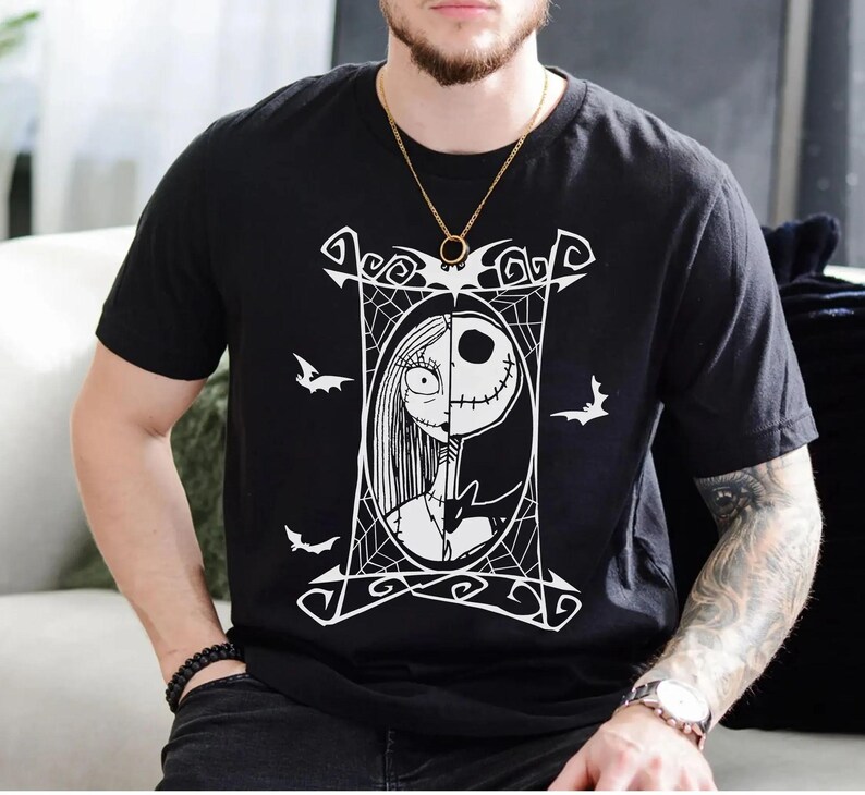 May include: Black t-shirt featuring a white graphic of Jack Skellington and Sally from The Nightmare Before Christmas. The design is framed by a decorative border with bats and spiderwebs. A gold chain necklace is visible.