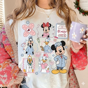 Puede incluir: Camiseta color crema con personajes de dibujos animados con atuendos m&eacute;dicos. El dise&ntilde;o incluye Minnie Mouse, Mickey Mouse, Donald Duck, Goofy y Daisy Duck, junto con s&iacute;mbolos m&eacute;dicos y la palabra "Nurse".