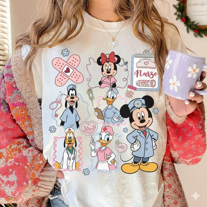 Puede incluir: Camiseta color crema con personajes de dibujos animados con atuendos m&eacute;dicos. El dise&ntilde;o incluye Minnie Mouse, Mickey Mouse, Donald Duck, Goofy y Daisy Duck, junto con s&iacute;mbolos m&eacute;dicos y la palabra "Nurse".