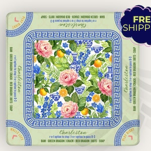 May include: A square decorative item with a floral design featuring pink roses, blue flowers, and oranges. The item has a blue and white border with the word "Charleston" and other text. The item is on a light green background.