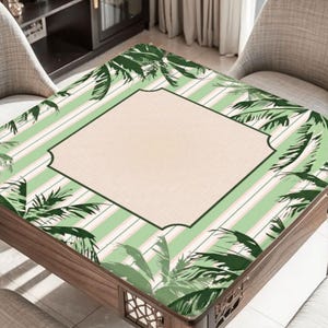 K&ouml;nnte beinhalten: Ein Holztisch mit dekorativer Tischplatte mit tropischem Design. Die Tischoberfl&auml;che hat ein hellgr&uuml;nes und wei&szlig; gestreiftes Muster mit Palmenillustrationen. Die Mitte hat einen beigefarbenen, gerahmten Bereich.