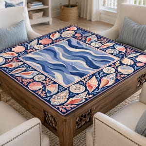 K&ouml;nnte beinhalten: Ein quadratischer Couchtisch aus Holz mit einer marineblauen Oberfl&auml;che mit einem Muschel- und Wellenmuster. Der Tisch ist von vier wei&szlig;en Sesseln mit blauen Kissen umgeben, was ein K&uuml;stenmotiv erzeugt.