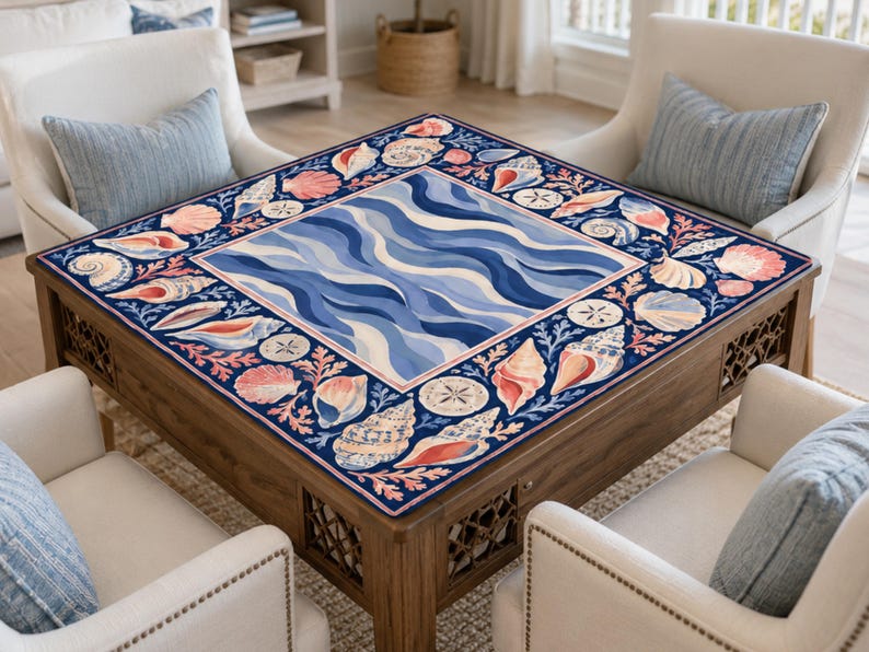 K&ouml;nnte beinhalten: Ein quadratischer Couchtisch aus Holz mit einer marineblauen Oberfl&auml;che mit einem Muschel- und Wellenmuster. Der Tisch ist von vier wei&szlig;en Sesseln mit blauen Kissen umgeben, was ein K&uuml;stenmotiv erzeugt.