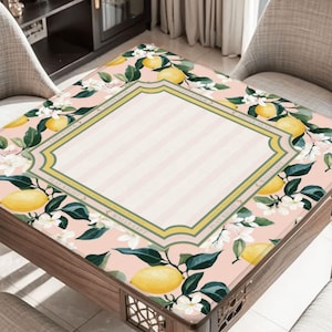 May include: A wooden table with a decorative floral tablecloth featuring lemons, white flowers, and green leaves. The tablecloth has a pink background with a striped center and a decorative border.