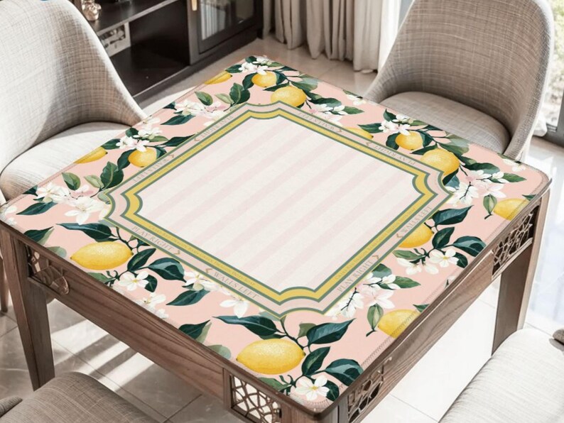 May include: A wooden table with a decorative floral tablecloth featuring lemons, white flowers, and green leaves. The tablecloth has a pink background with a striped center and a decorative border.