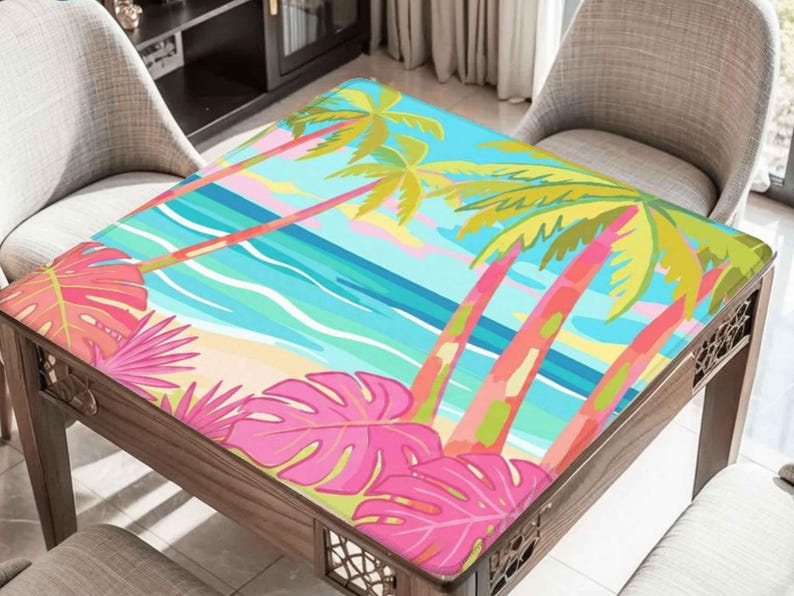 May include: A wooden table with a colorful tropical beach scene printed on the top. The design features palm trees, pink and green leaves, a sandy beach, and blue ocean waves. The table is surrounded by two chairs.