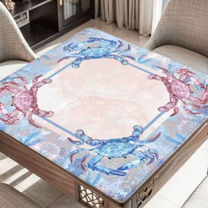 Puede incluir: Mesa cuadrada de madera con dise&ntilde;o de cangrejos. La mesa presenta un patr&oacute;n de cangrejos azul claro y rosa sobre un fondo rosa claro y azul. La mesa est&aacute; rodeada de dos sillas.