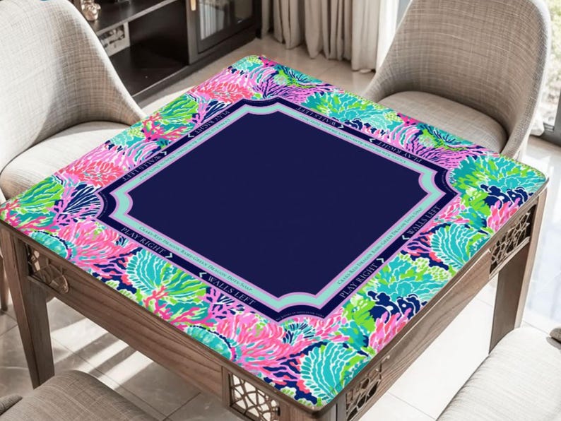 Puede incluir: Una mesa de cartas de madera con un centro azul marino y un borde floral colorido en rosa, verde y azul. La mesa tiene un borde decorativo y est&aacute; rodeada de dos sillas.